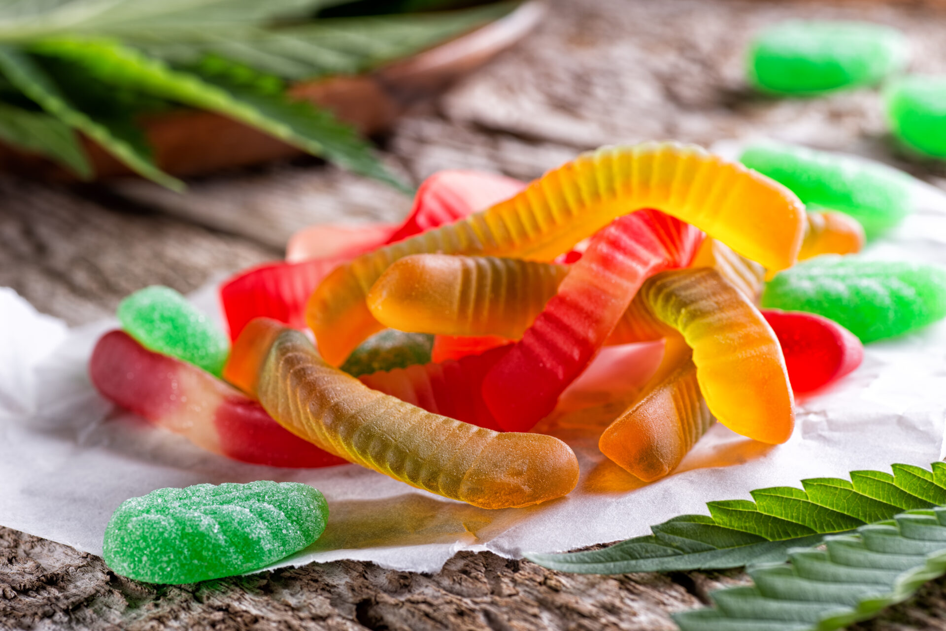 Cannabis infused gummy candy on a rustic table top with marijuana leaves.